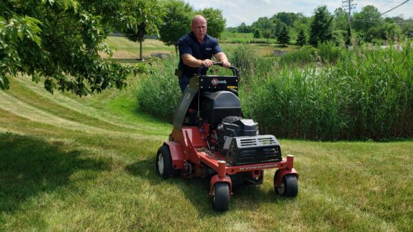 A man using a commercial lawn mower to maintain a large green lawn, illustrating a commercial lawn care bidding strategy.