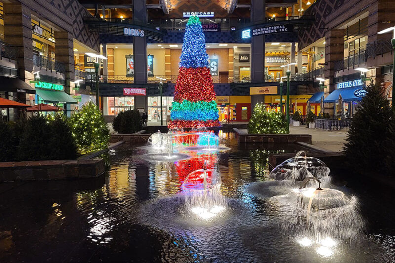 A magnificent Giant Christmas tree, bedecked with sparkling lights, stands as the centerpiece of a shopping center, beautifully capturing the festive spirit.