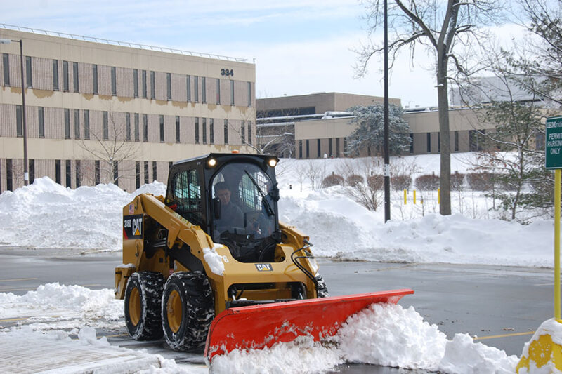 A proficient worker from a Connecticut commercial property management company operates a snow machine, effectively pushing snow aside outside the property. 
