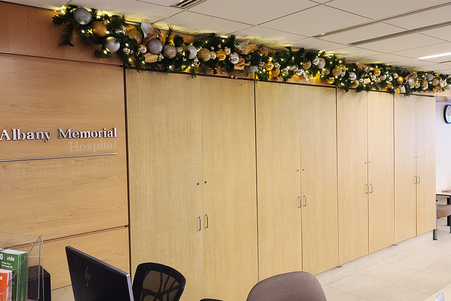 Holiday decorating services featuring garland with ornaments and lights above cabinets at Albany Memorial Hospital