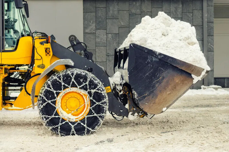 Loader machine piling snow in a safe area and making sure the runoff from melting snow will not refreeze on the pavement.