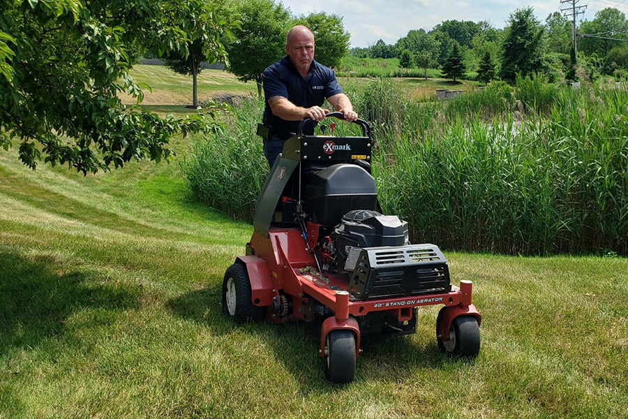 Man using a stand-on lawn aerator to maintain commercial property, showing how landscaping can improve safety and security on your property