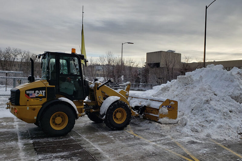 Snow plow operator clearing snow from a commercial property with heavy-duty snow plow machine